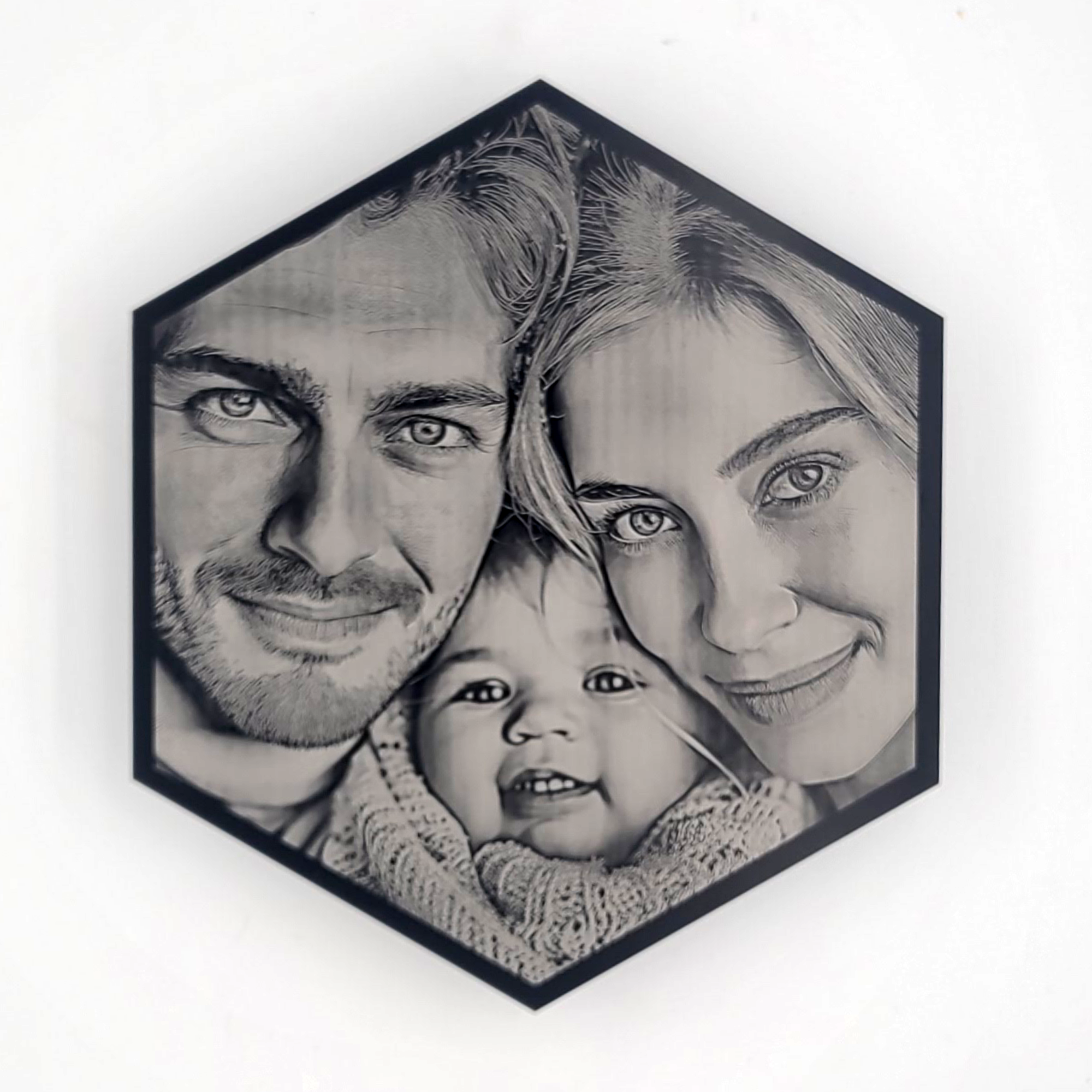 Hexagonal black-and-white portrait of a smiling family with two adults and a baby.